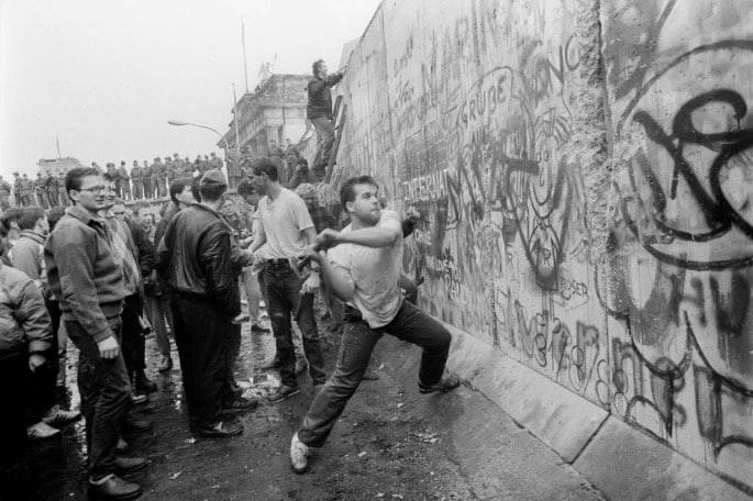 Ciudadanos derriban el muro con mazos observados por soldados al fondo